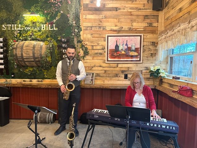 A man is playing a saxophone and a woman is playing a keyboard in a room.