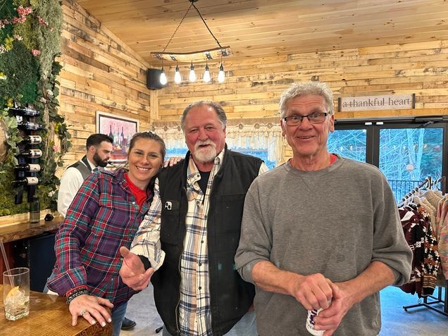 Three people are posing for a picture in a room with wooden walls.