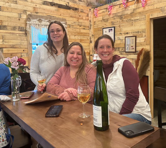 Three women are sitting at a table with a bottle of wine