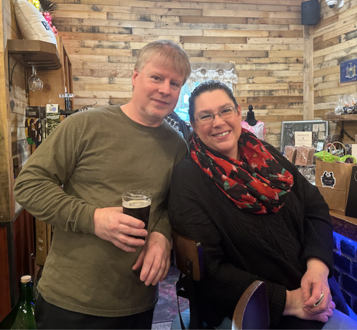 A man and a woman are posing for a picture and the man is holding a glass of beer