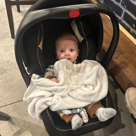 A baby is sitting in a car seat wrapped in a blanket.