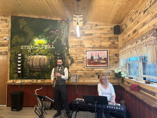 A man is playing a saxophone and a woman is playing a keyboard in a room with wooden walls.