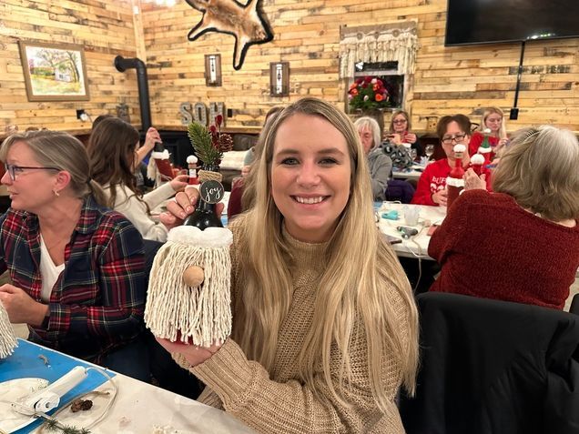 A woman is sitting at a table holding a gnome.