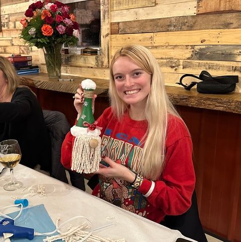 A woman in a red sweater is sitting at a table holding a christmas ornament.