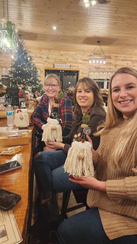 Three women are sitting at a table holding christmas decorations.