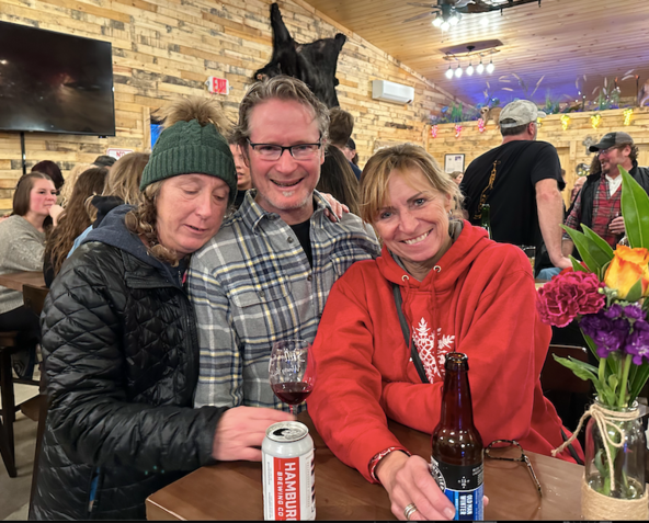 A man and two women are sitting at a table with a can of scar beer