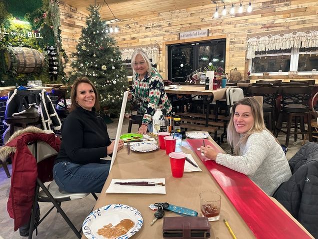 Three women are sitting at a table in a room with a christmas tree in the background.