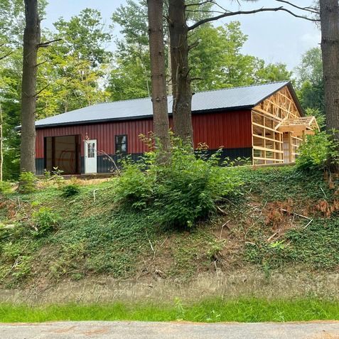A red barn is being built on a hill in the woods.