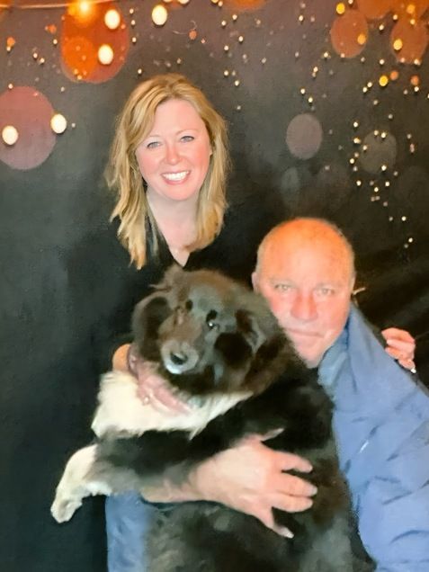 A man and a woman are holding a black dog