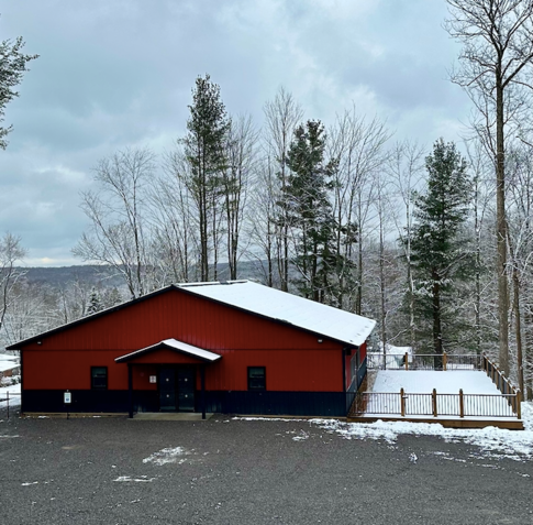 A red building with snow on the roof and trees in the background