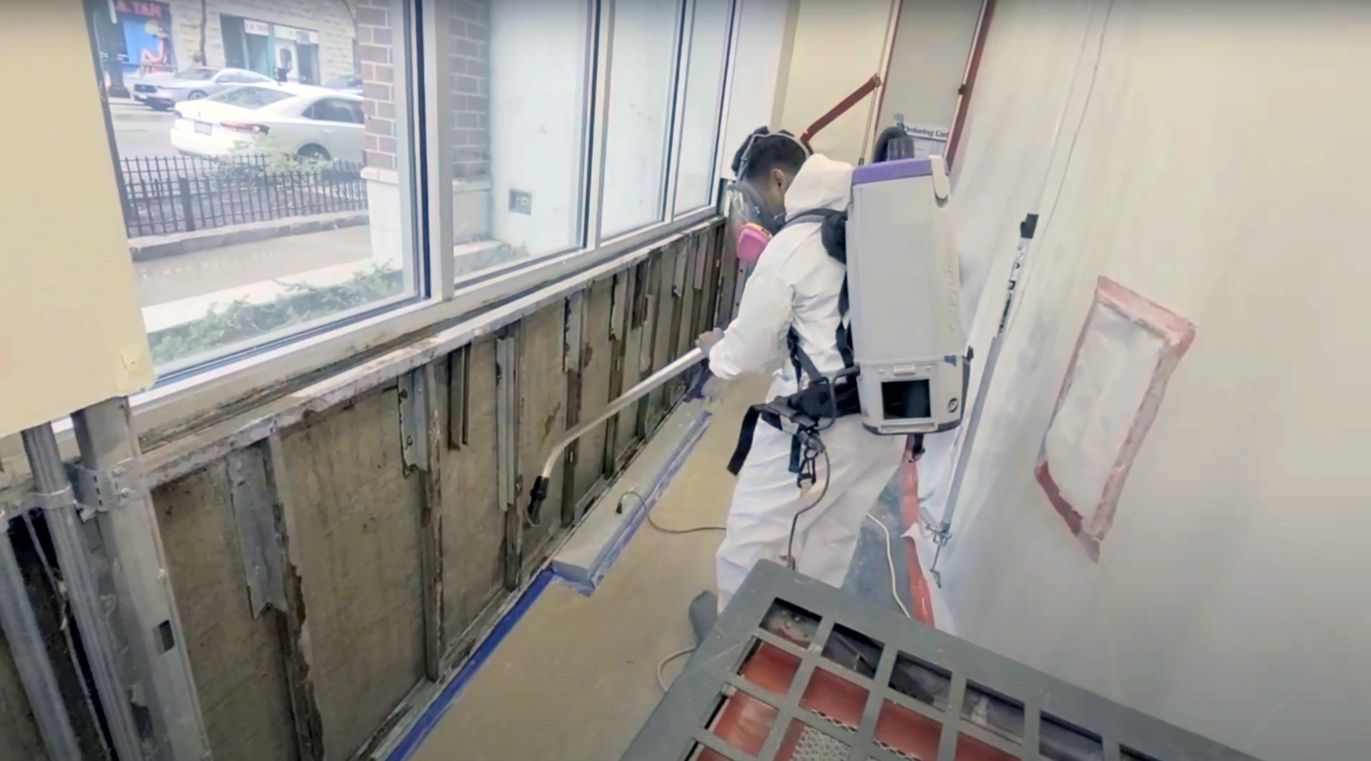 Technician in a Tyvek suit and chemical respirator spraying exposed moldy walls with Concrobium in a commercial building in Carlsbad, California.