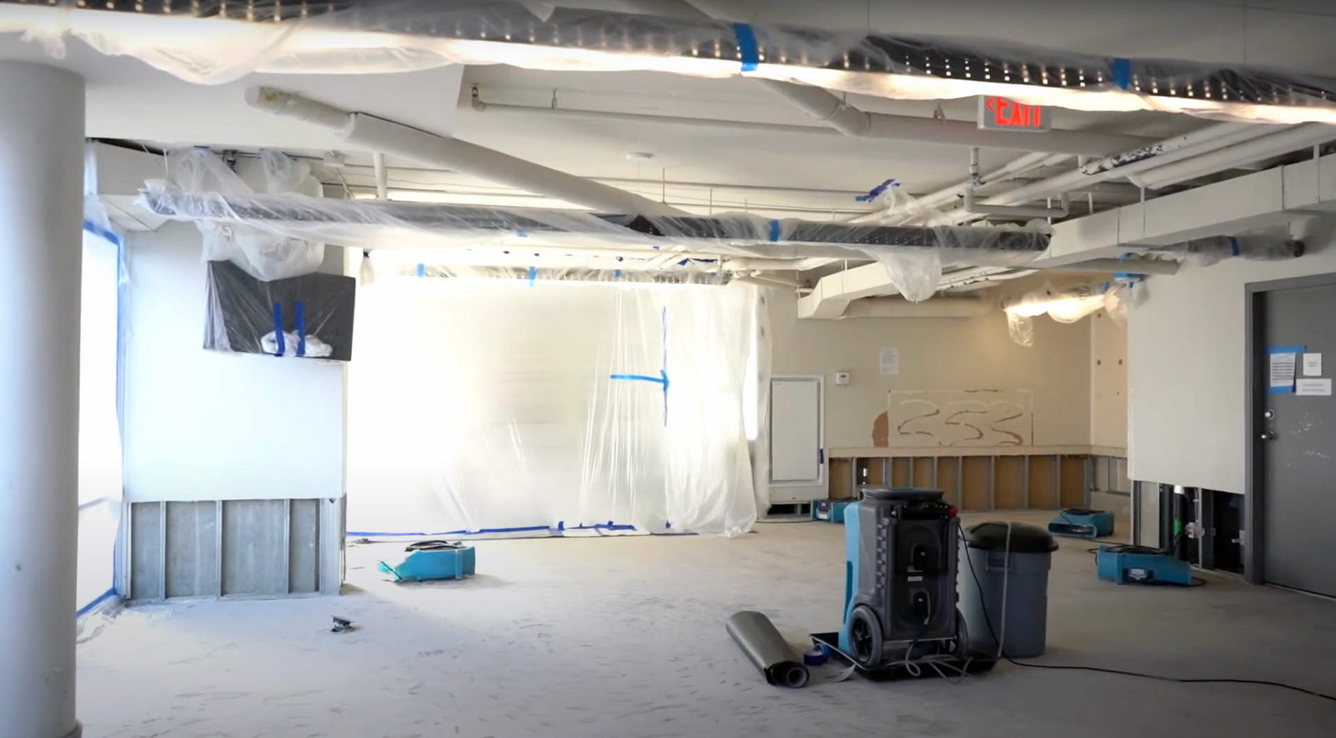 Interior office of a commercial building in Carlsbad, CA, prepped for water damage restoration with polyethylene containment sheeting, HEPA air scrubbers, and LGR dehumidifiers throughout the space.