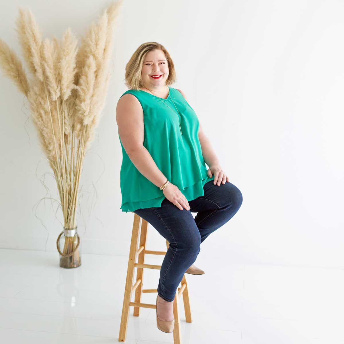 Andi Dyer wearing a tan jacket and a red shirt is standing in the grass.