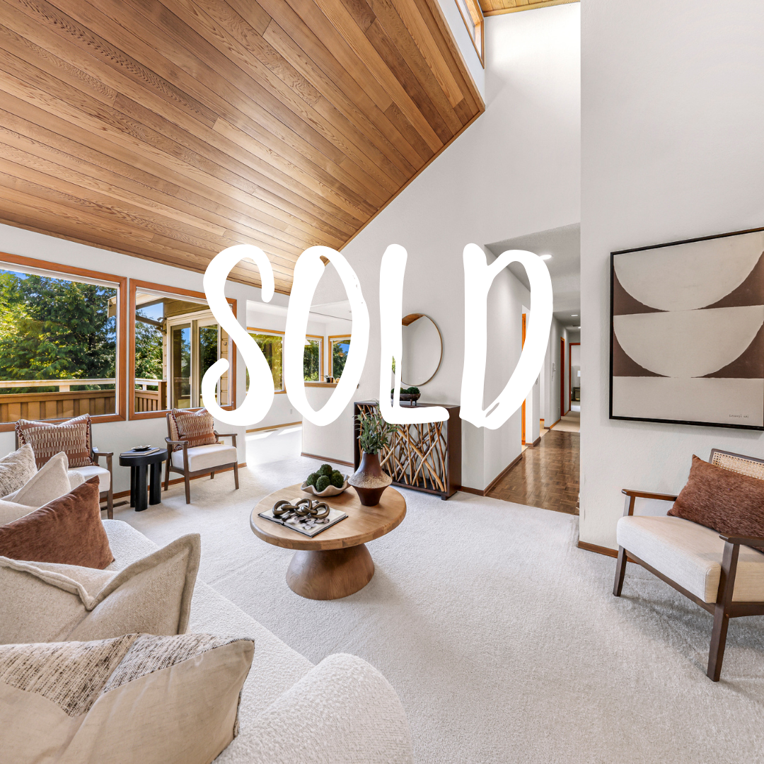 Spacious living room features vaulted cedar ceilings, large windows, and soft carpeting for cozy comfort. A neutral palette and thoughtful staging highlight its welcoming ambiance.