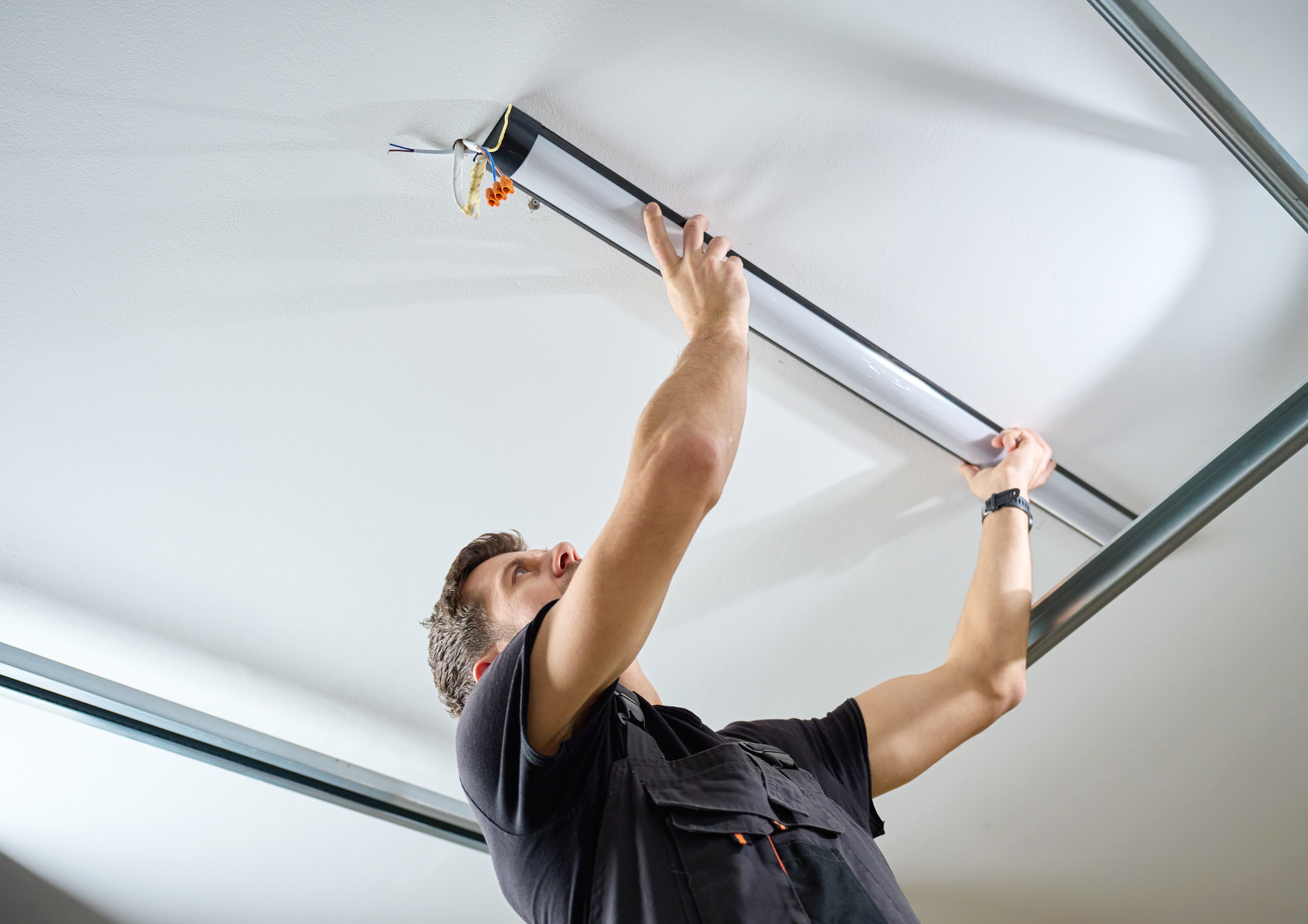 A person wearing a dark shirt installs a long, slim LED light fixture onto a white ceiling.