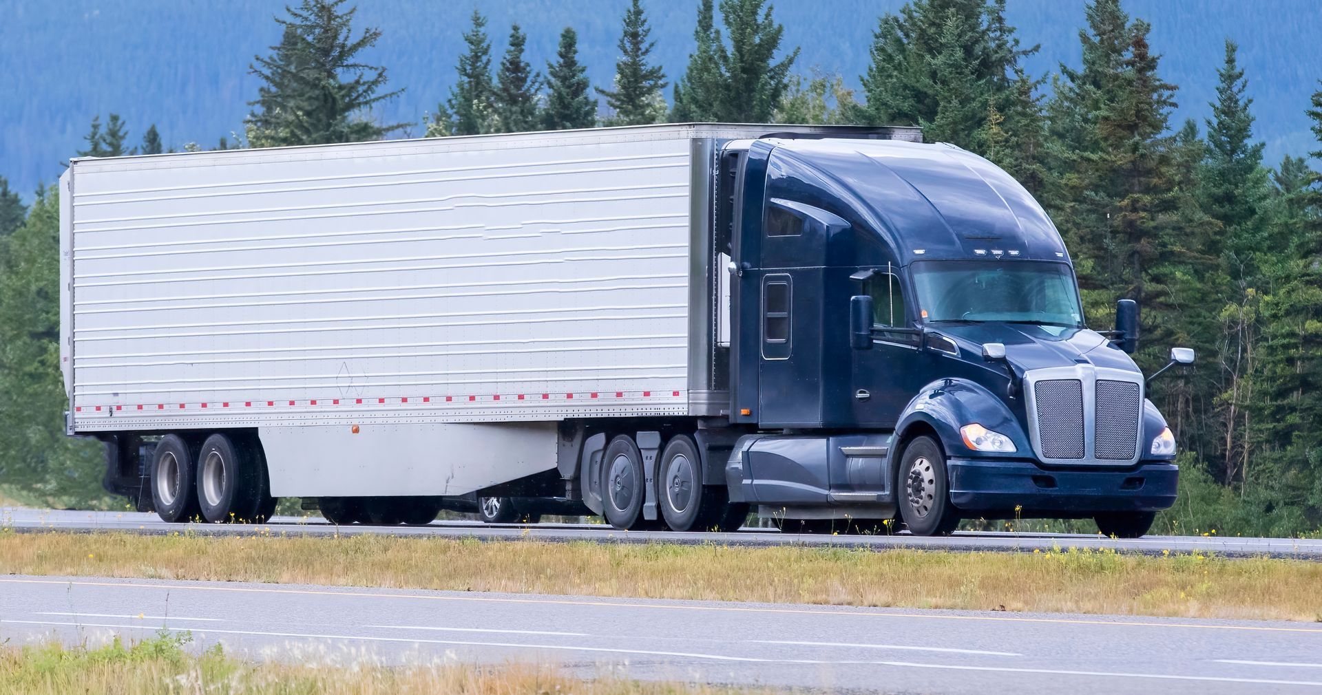 A semi truck with a white trailer is driving down a highway.
