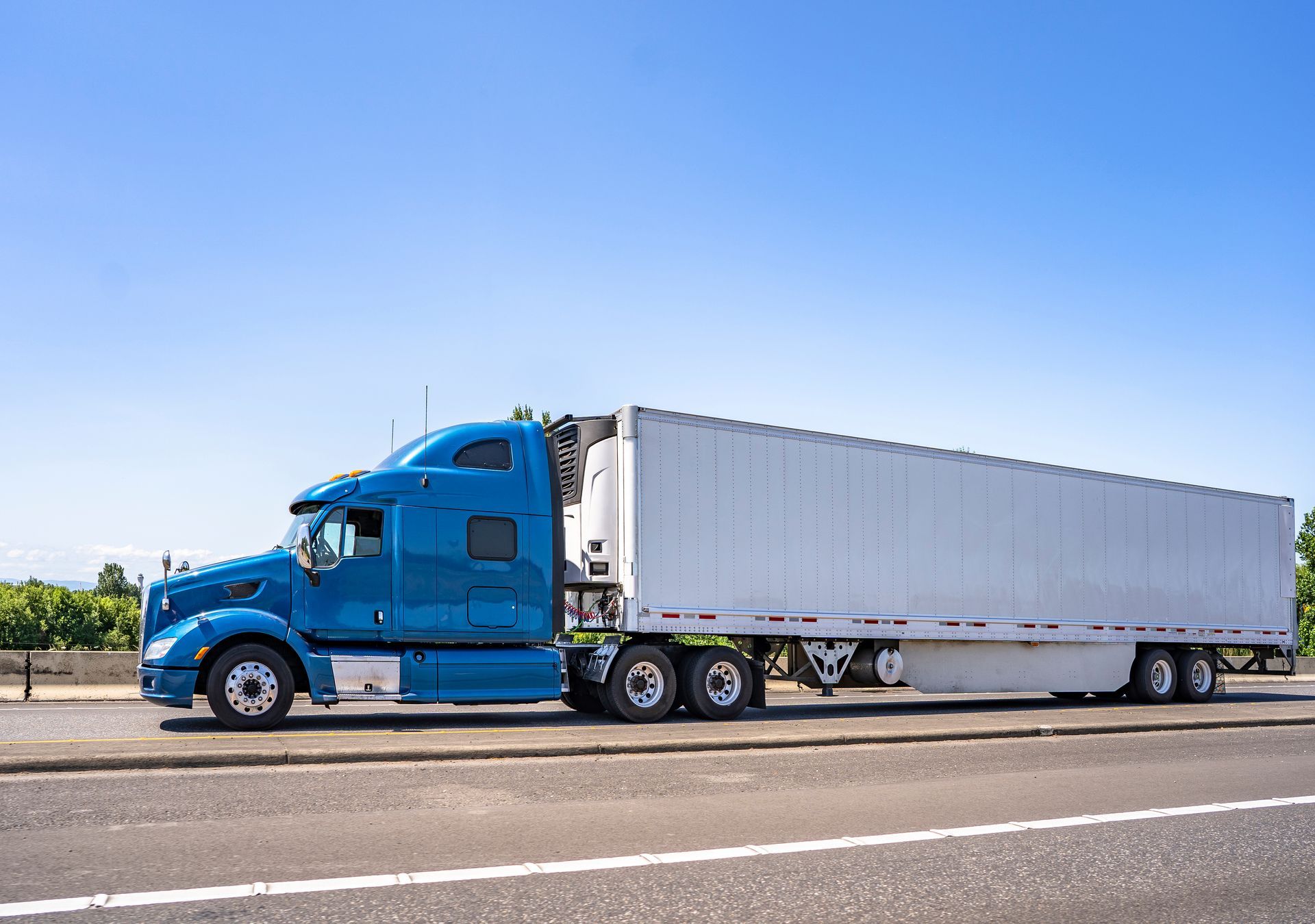 A blue semi truck with a white trailer is driving down a highway.