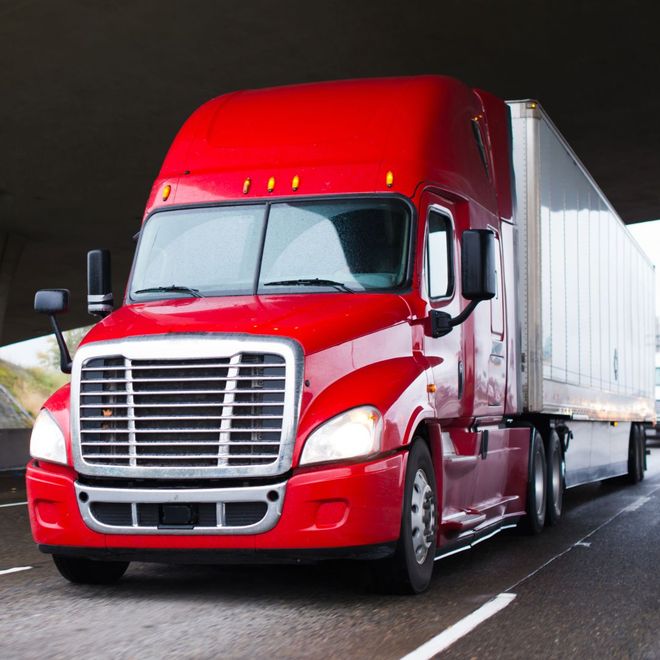 A red semi truck is driving down a highway under a bridge