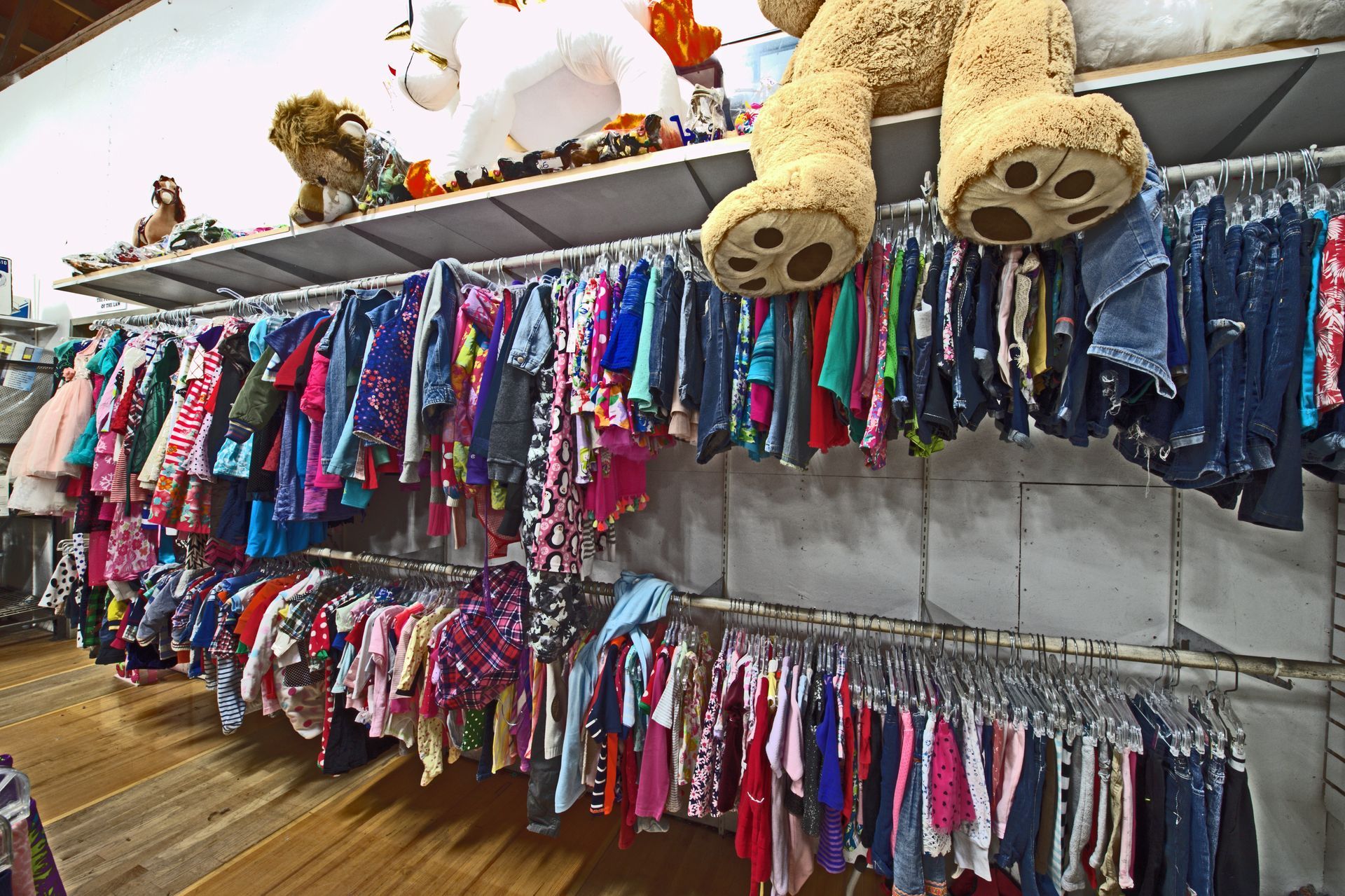 A teddy bear is sitting on a shelf in a clothing store.