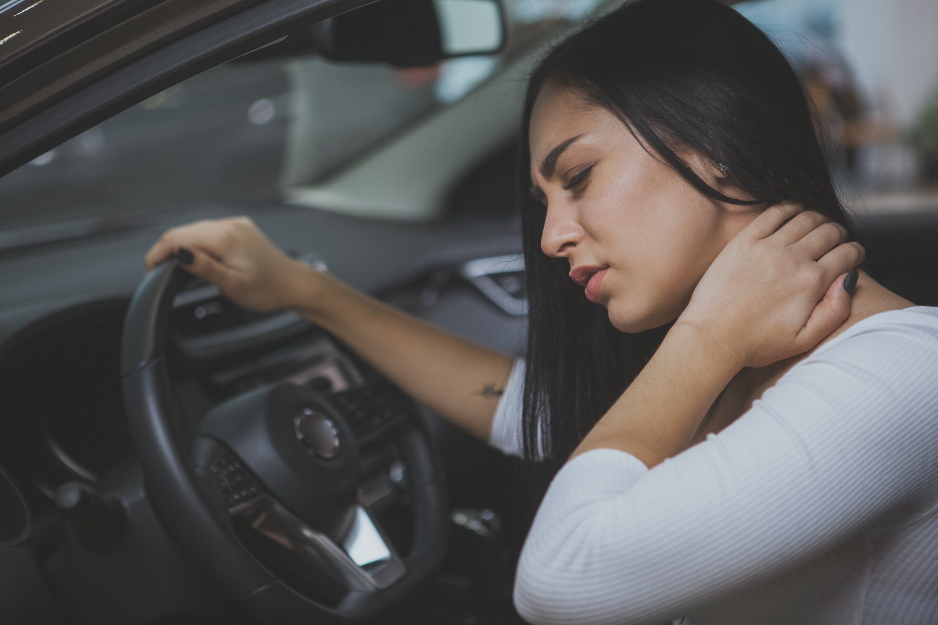 A woman is sitting in a car holding her neck in pain.