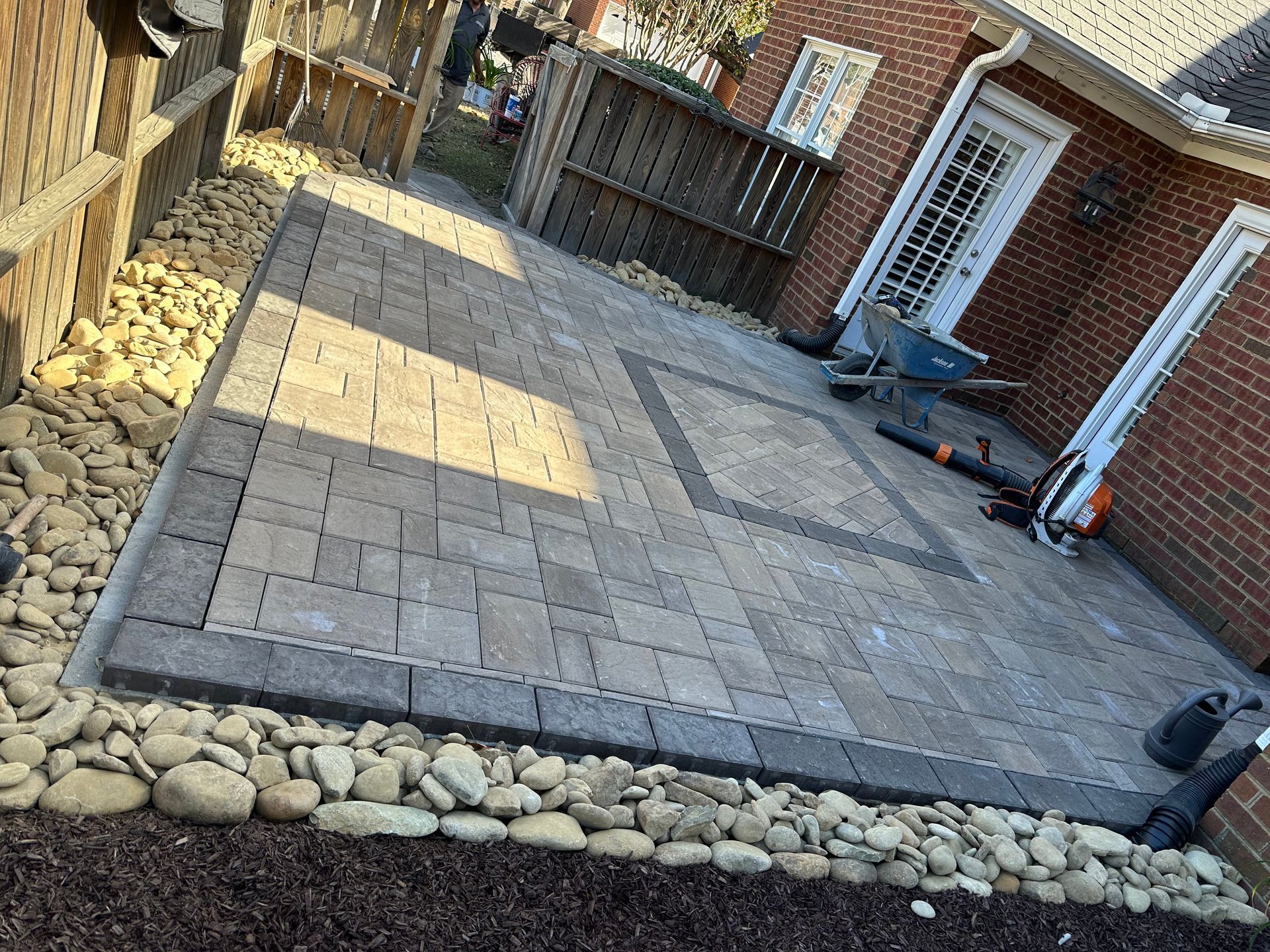 A paved patio with a border of rocks and a brown fence in the background.