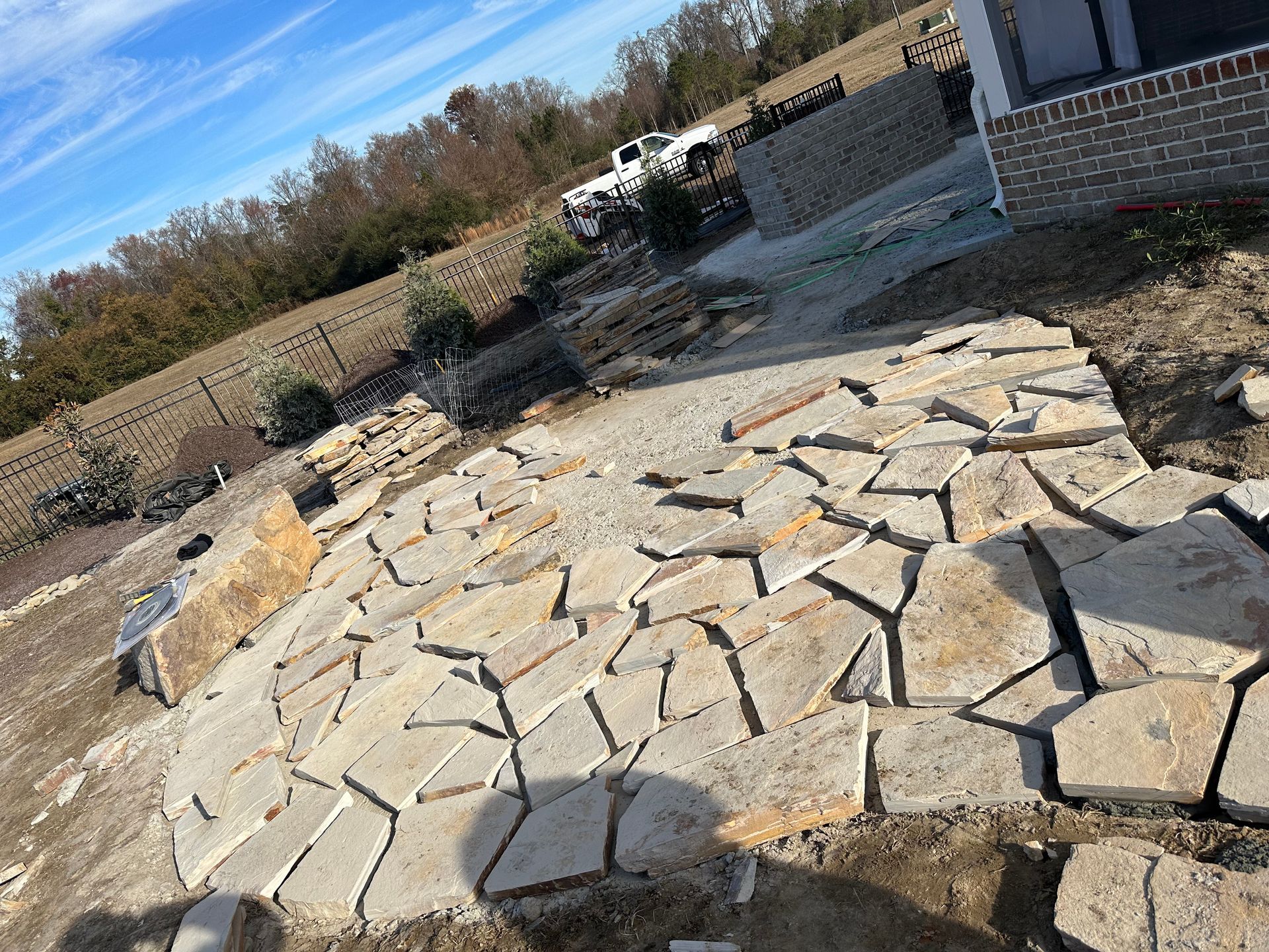 Stone pavers being installed in a yard near a house. Sky is blue with clouds.