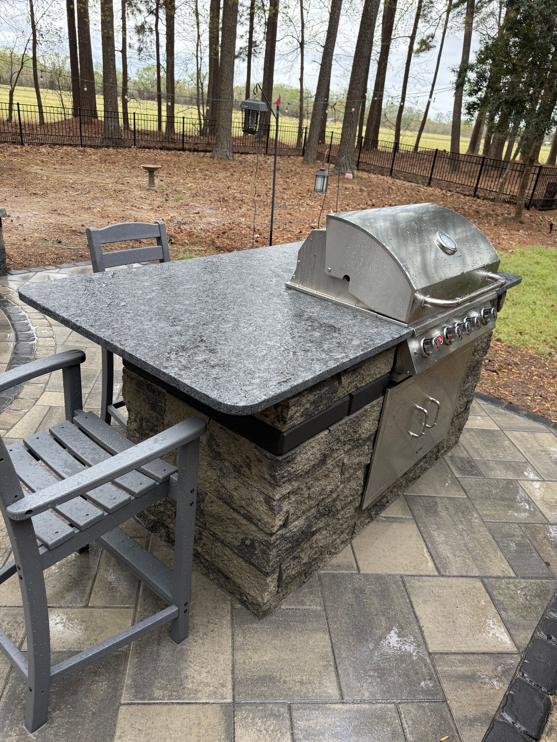 Outdoor grilling station with stainless steel grill, stone countertop, seating on a brick patio.