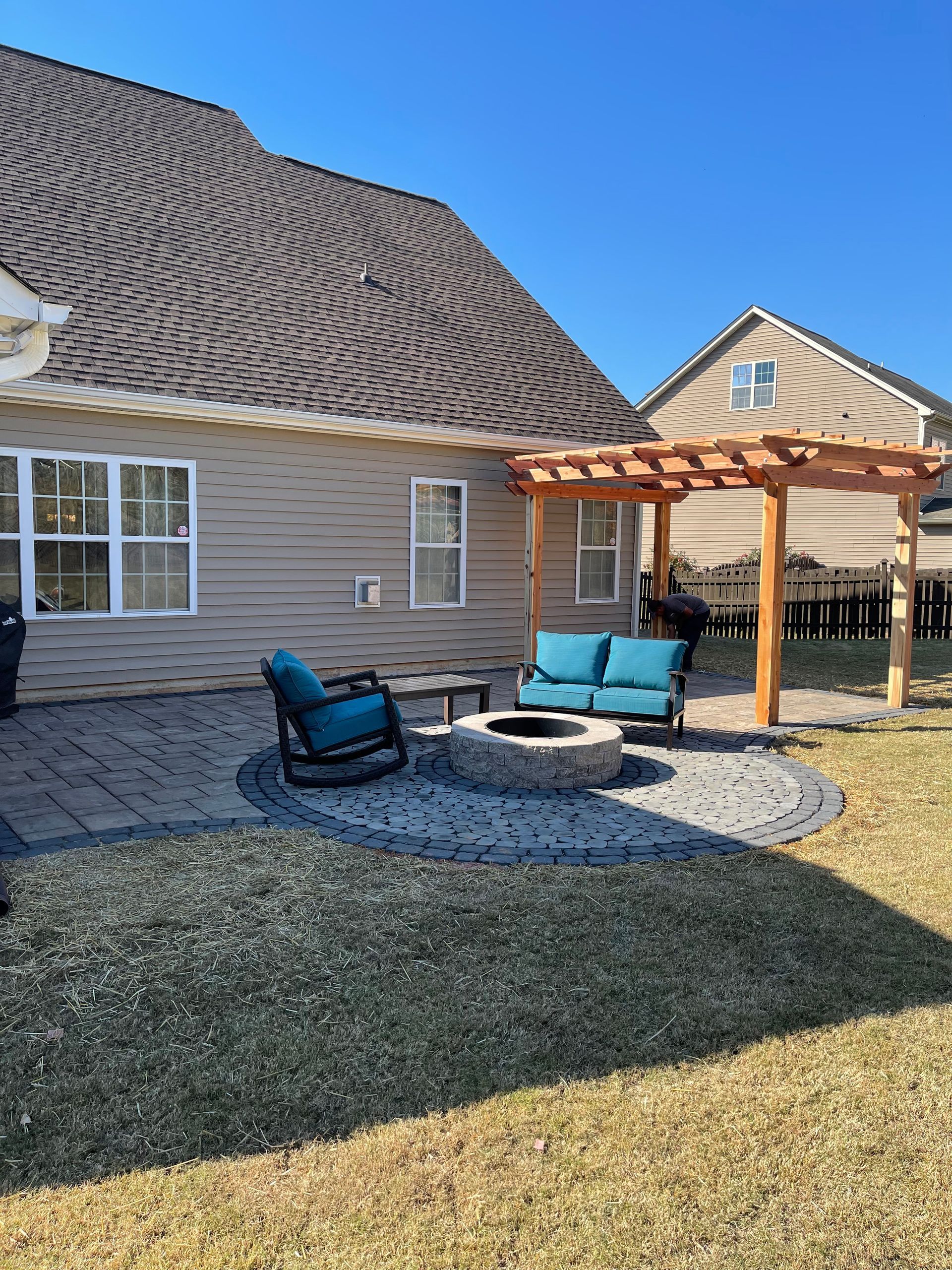 Backyard patio with fire pit, blue furniture, pergola, and house.