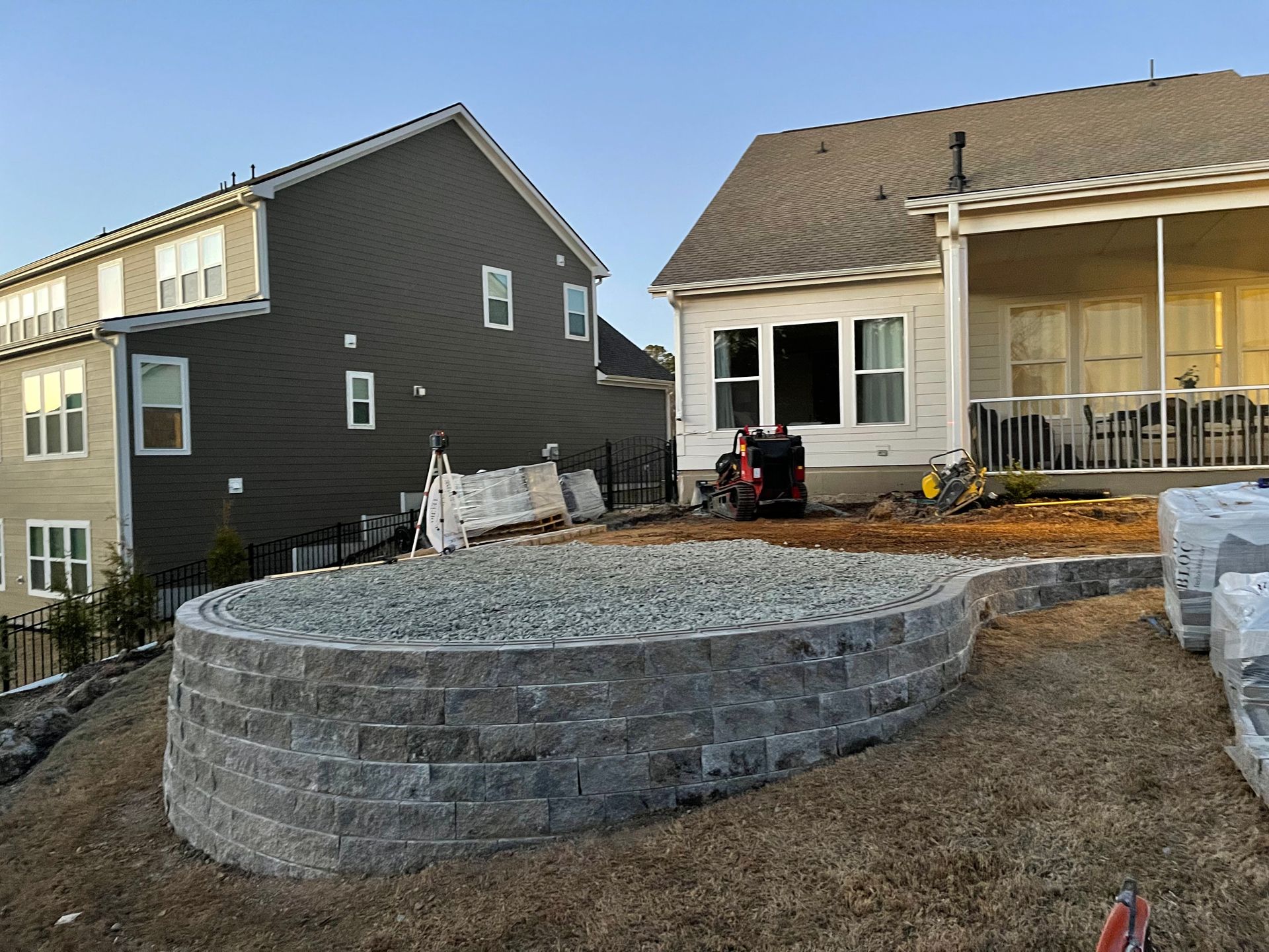 Low retaining wall made of gray bricks, filled with gravel, in a backyard. Houses visible in the background.