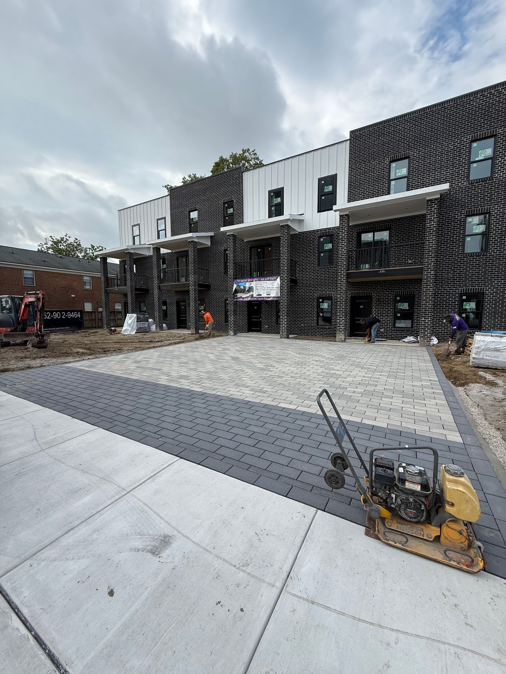 Newly constructed multi-unit building with brick facade and paving stones being installed.