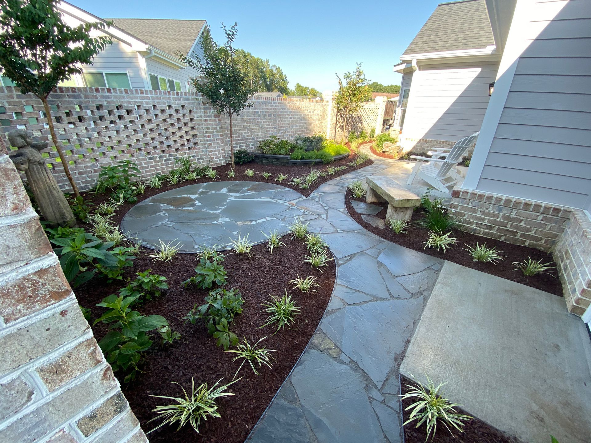 A landscaped backyard with a stone patio, brick walls, and various plants.
