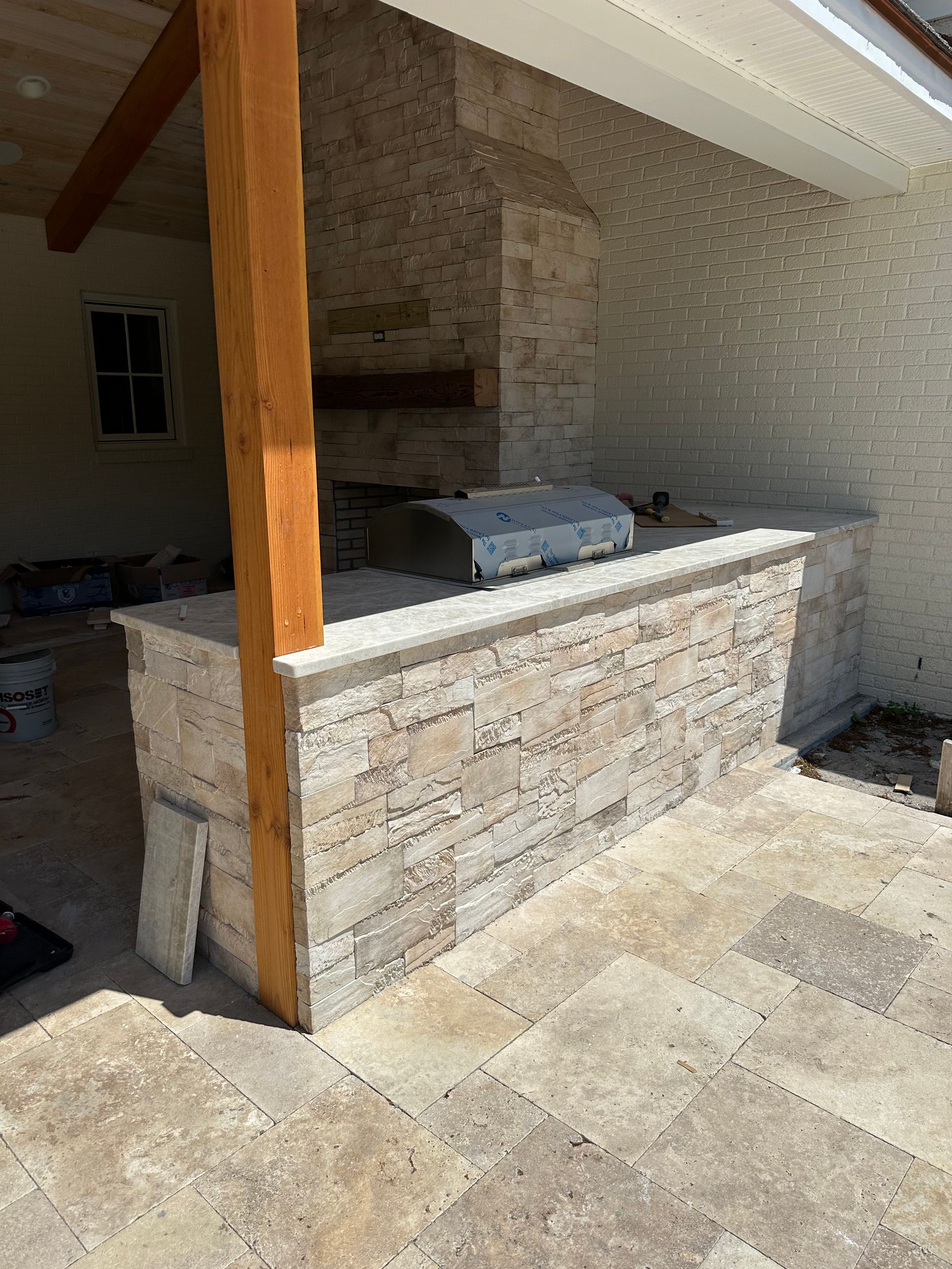 Outdoor kitchen with stone facing, built-in grill, and bar under a wooden pergola.