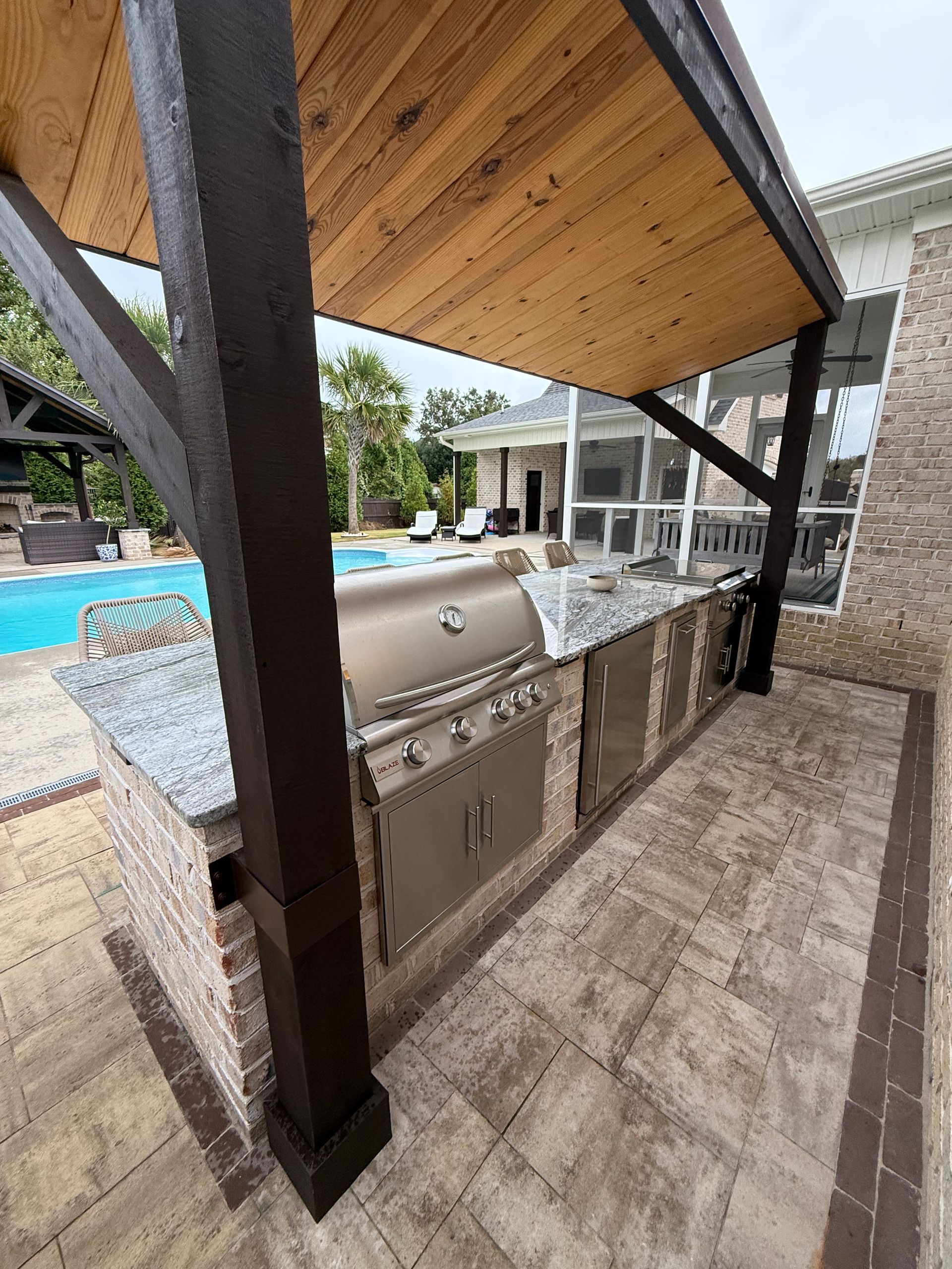 Outdoor kitchen with a grill, granite countertop, and wooden pergola.