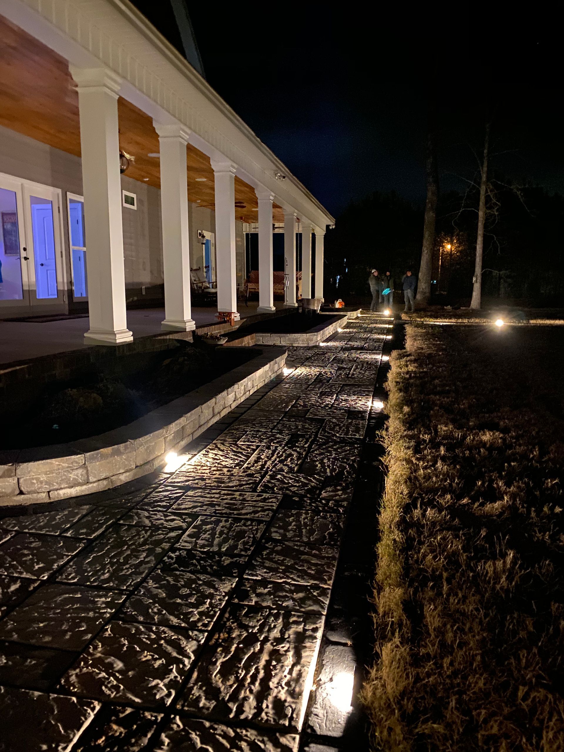 Pathway illuminated by lights alongside a building with white columns at night.