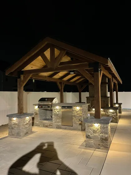 Outdoor grilling station with stainless steel grill, stone countertop, seating on a brick patio.