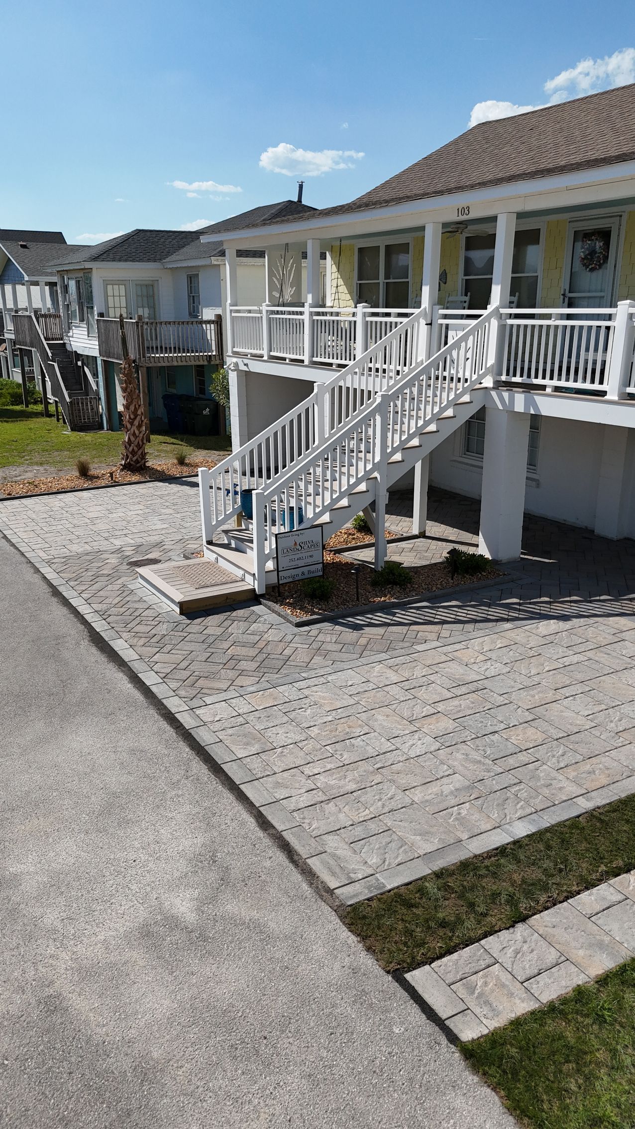 Beach house with exterior stairs, paved area, and blue sky.
