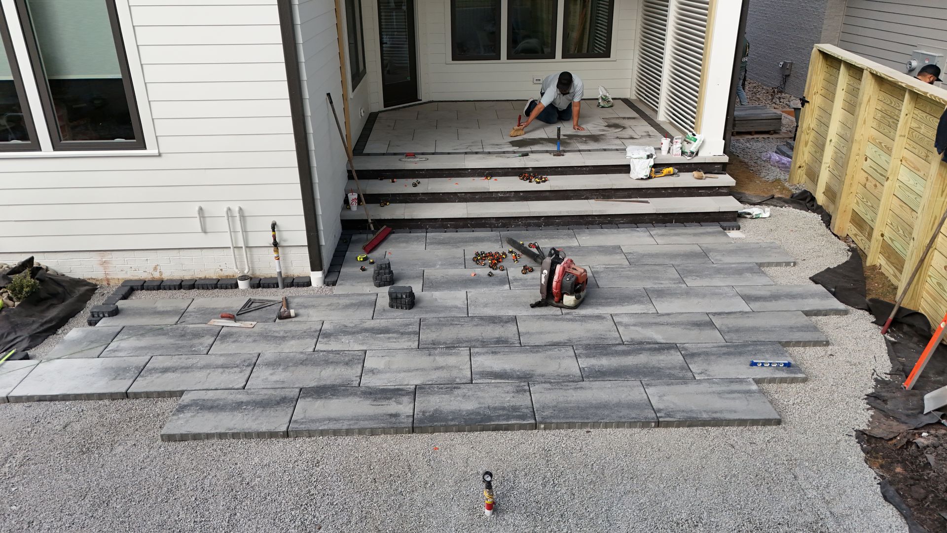 Construction of a patio with pavers; worker laying stones. Gray pavers being installed near a house.
