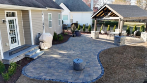 Backyard patio with stone pavers, gazebo, and grill. House exterior in background.