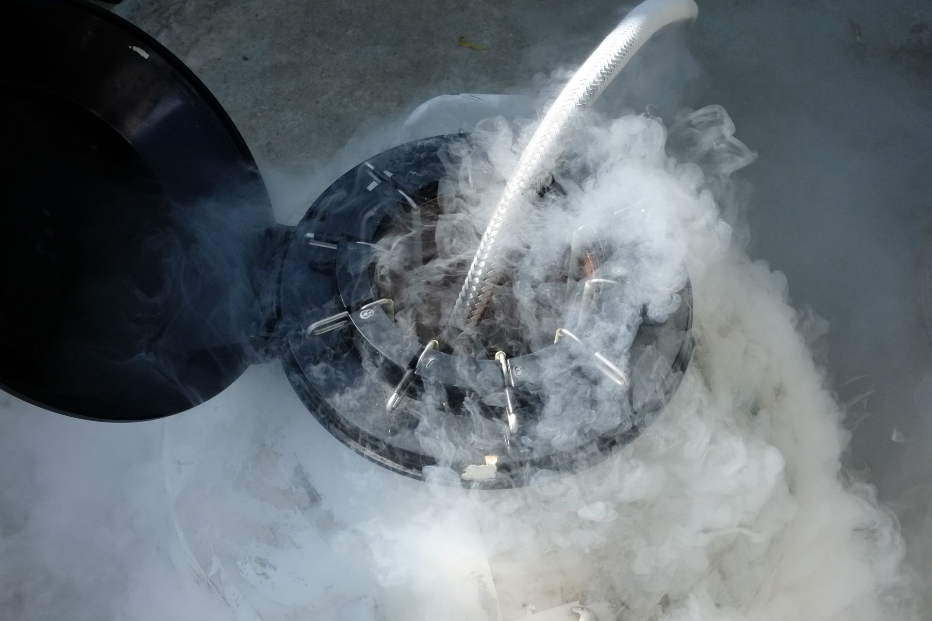 Liquid being poured into a smoking, dark-colored container, likely with frozen food.