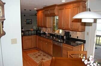 A kitchen with light wood cabinets, dark granite countertops, stainless steel appliances, and wood flooring.