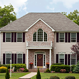 A two-story brick and siding house with a central balcony, arched window, and landscaped yard.