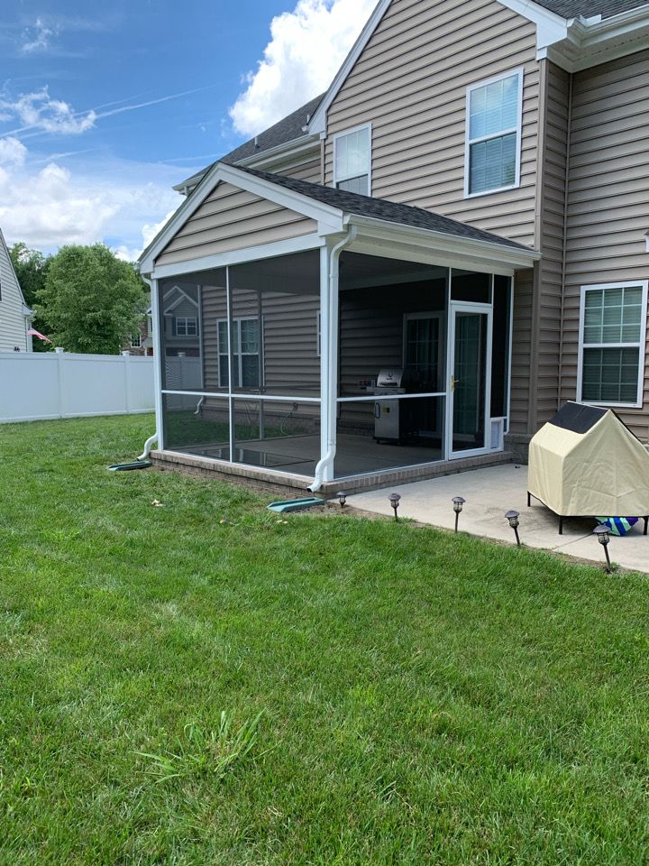 A screened-in patio attached to the back of a beige siding house, with a grassy yard and a small covered pet shelter.