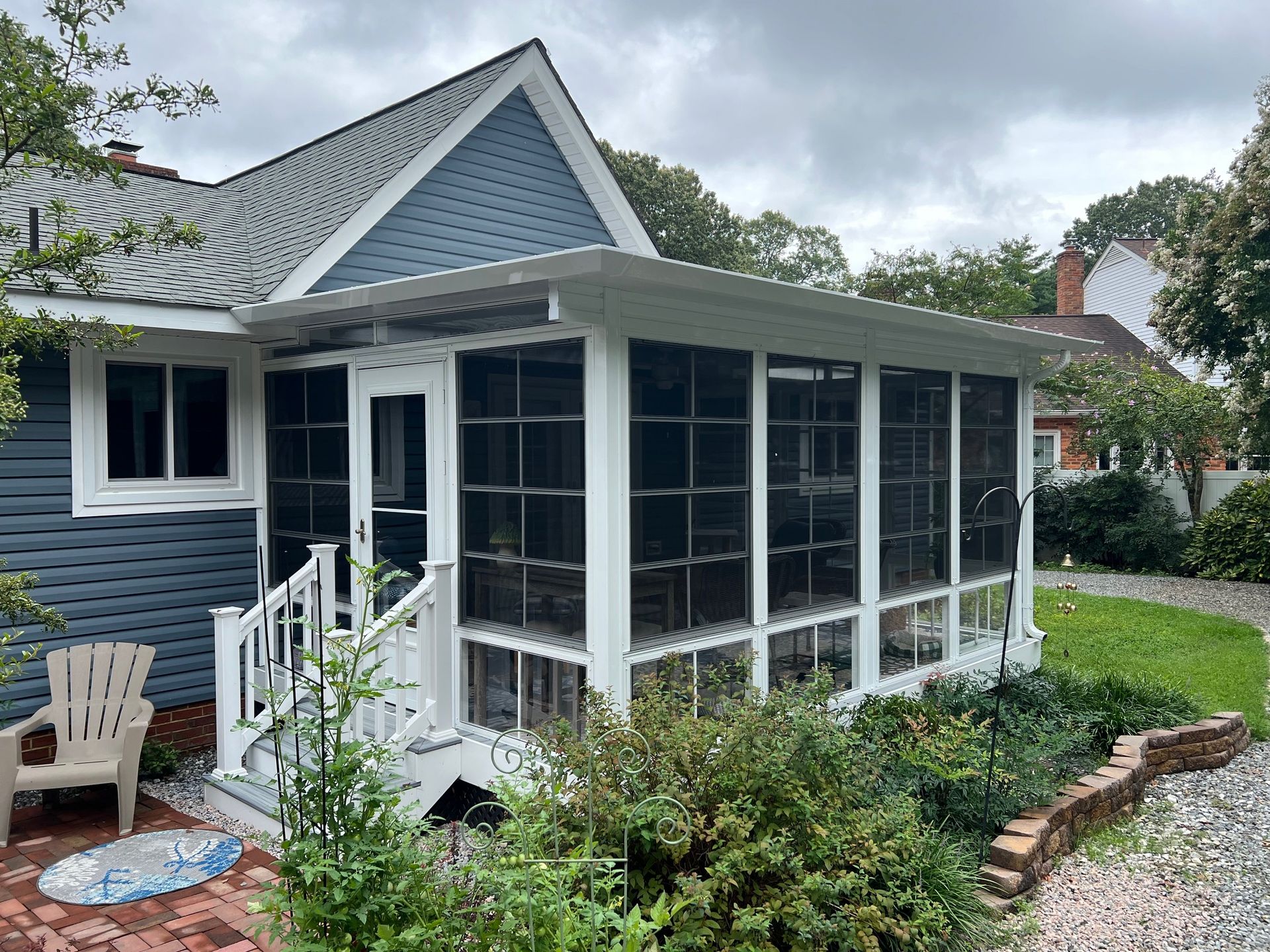 A blue house with white trim features an attached screened-in porch with stairs leading to a brick patio.