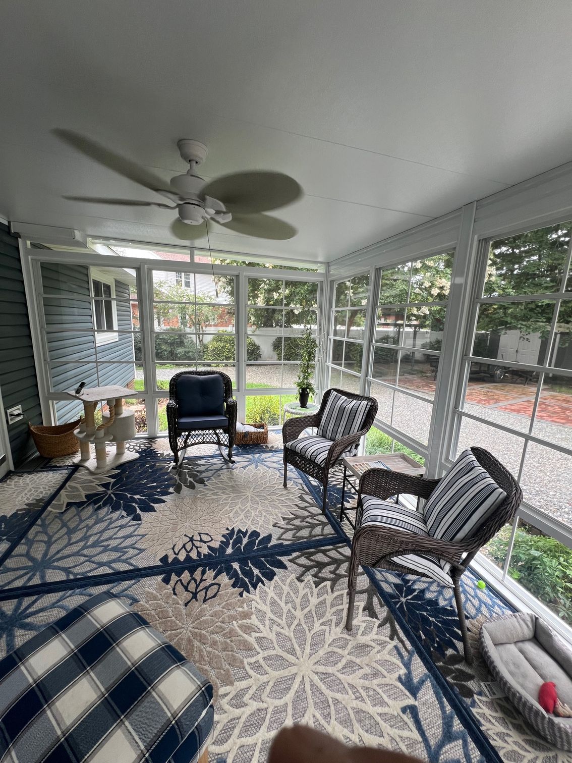 A screened-in porch with a patterned rug, three wicker chairs, a white side table, and a ceiling fan.