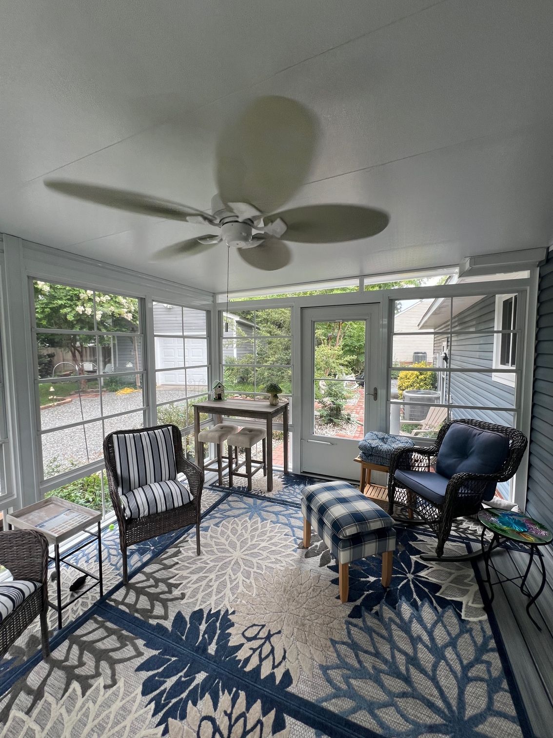 A screened-in porch with outdoor furniture, a ceiling fan, and a patterned blue-and-white area rug.