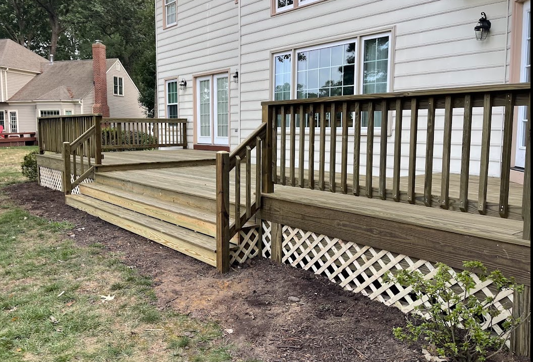 A two-level wooden deck with white lattice skirting and railings attached to the back of a light-colored house.