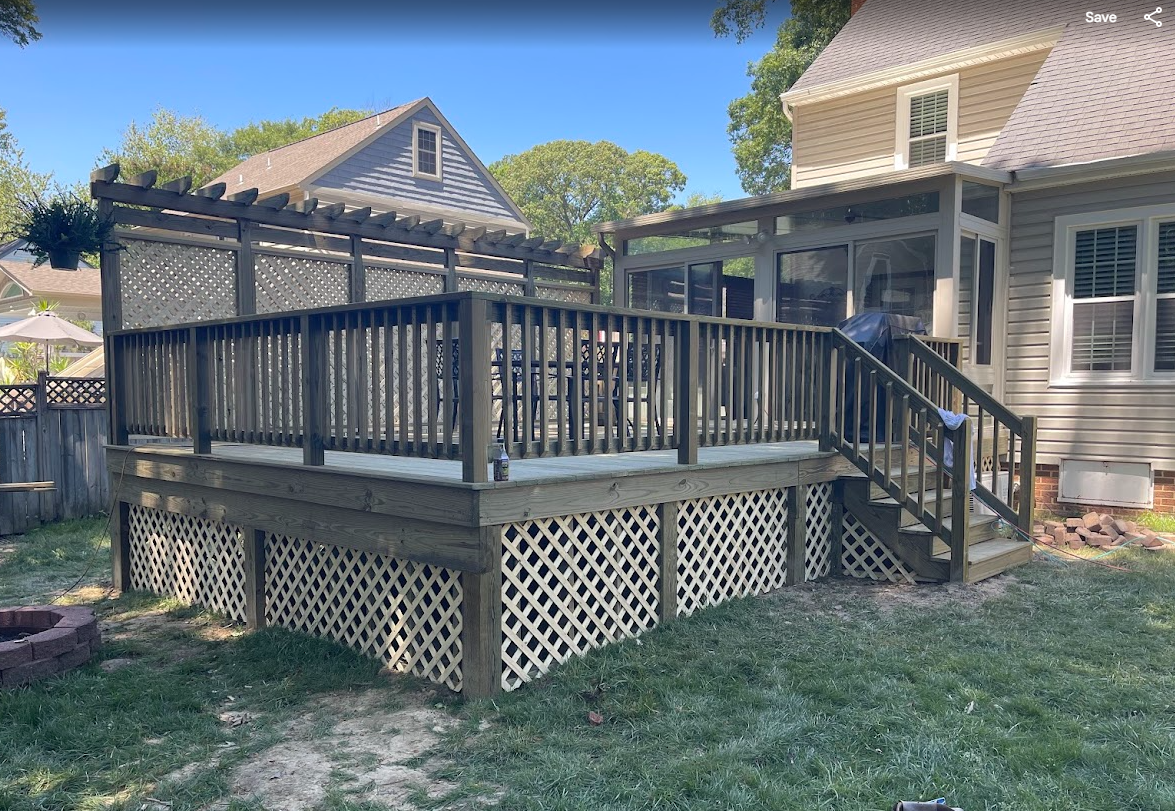 A wooden backyard deck with a trellis and lattice skirting attached to the rear of a light-colored two-story house.