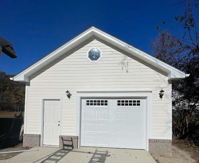 A detached, light-colored garage with white trim, a single-car door, a side entry door, and an octagonal accent window.