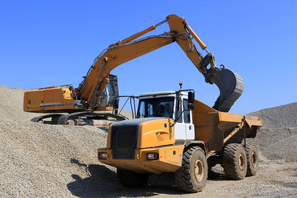 A Yellow Excavator is Loading a Dump Truck With Gravel — Hardy's Excavations in Round Mountain, NSW