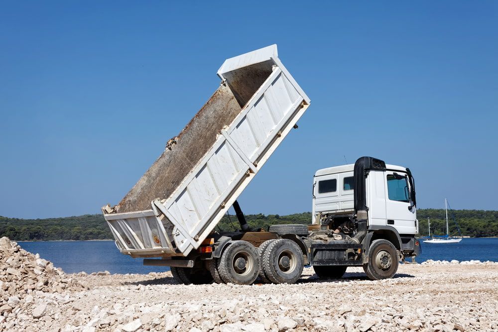 A Dump Truck is Driving Down a Dirt Road Next to a Body of Water — Hardy's Excavations in Pottsville, NSW